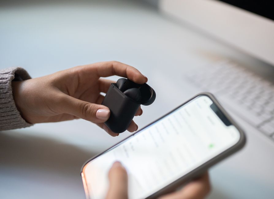 Hands connecting wireless earbuds to a smartphone via Bluetooth