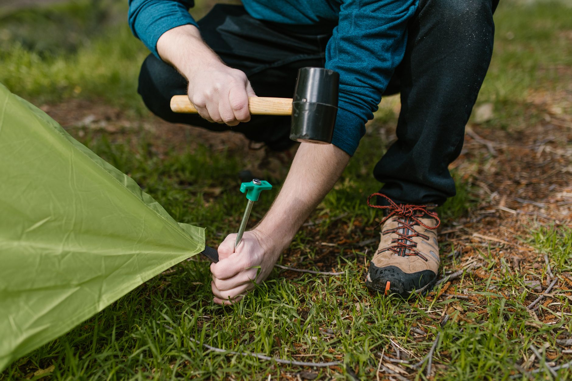 A person hammering a tent peg into the ground