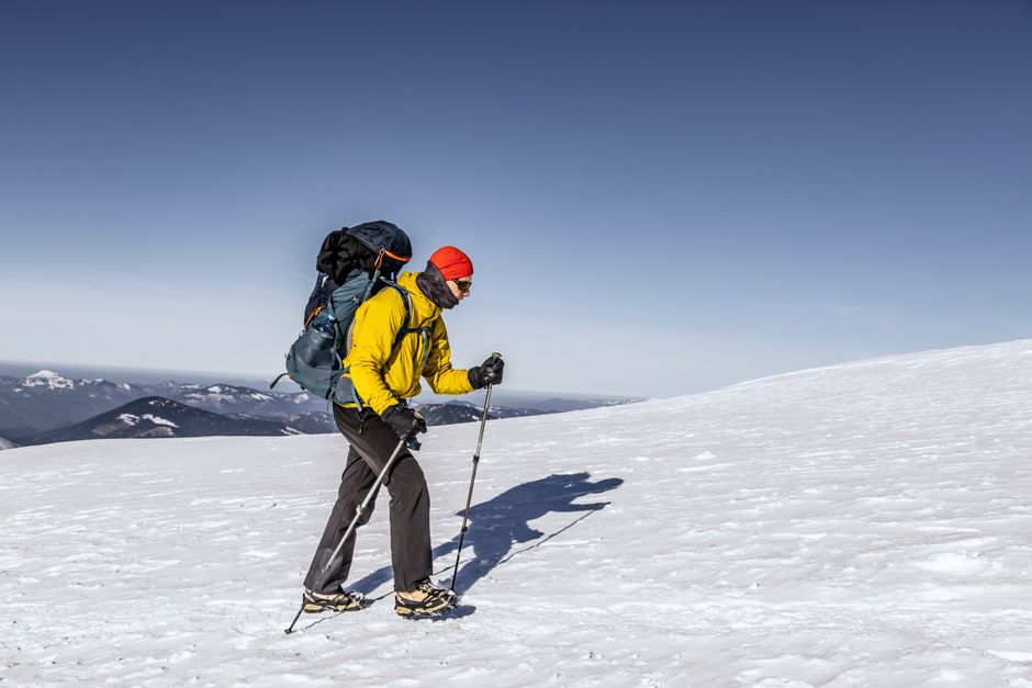 A hiker in layered winter gear ascending a snowy mountain