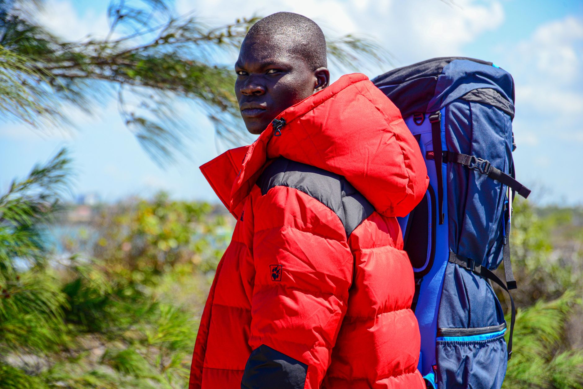 Man in a red jacket carrying a backpack and looking over his shoulder