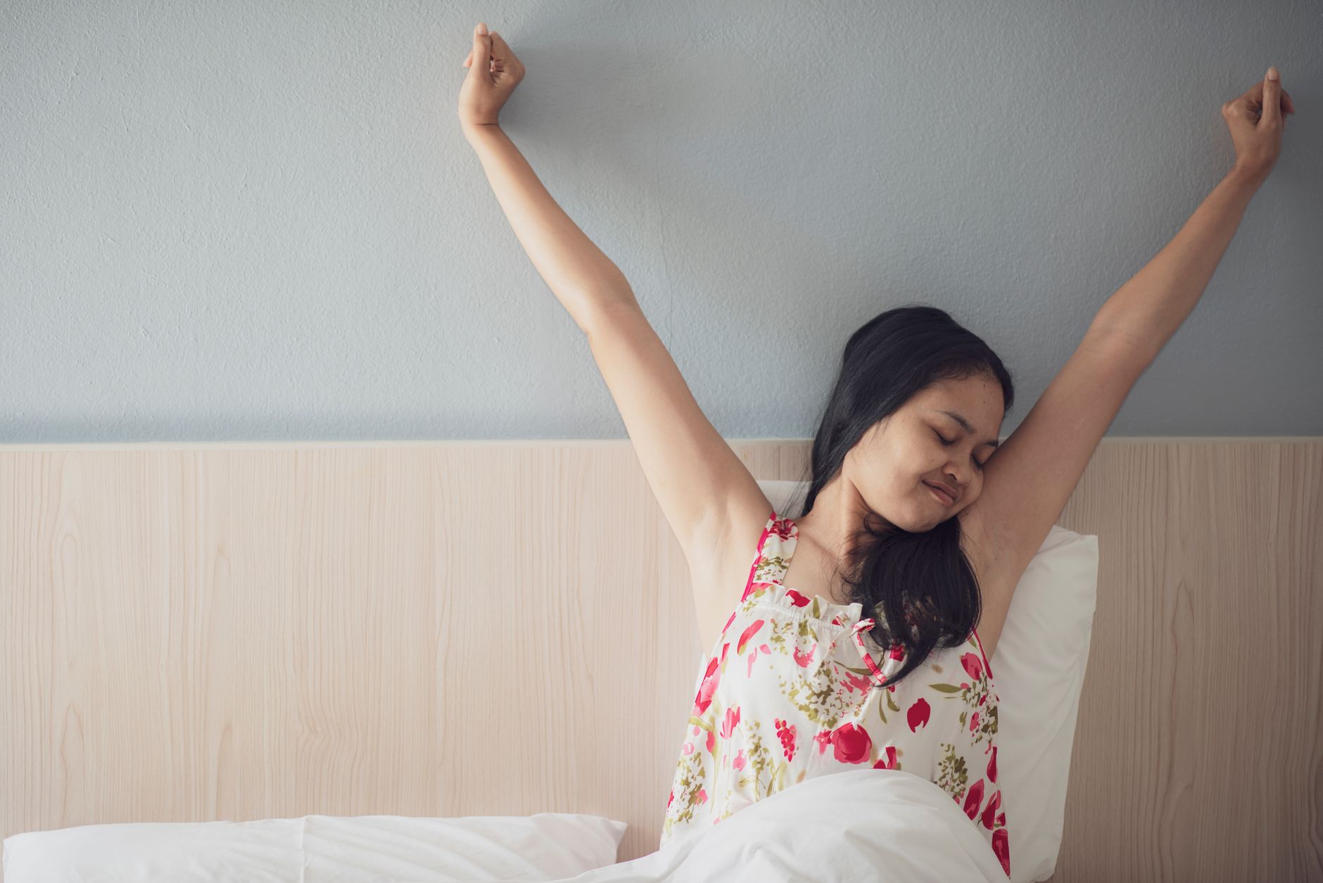 Woman stretching her arms while sitting on the bed in the morning