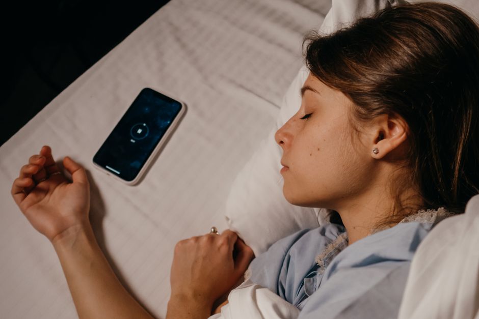 A smartphone resting beside a sleeping woman in bed